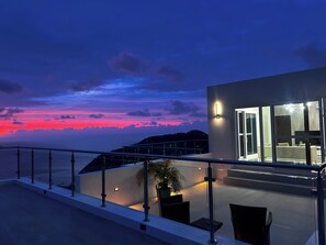 A modern building with a glass facade, outdoor seating area, and a view of the sunset over the water. - Zafira Luxe 1-bedroom villa with sauna, steam, sunset views, AC, WIFI in Tortola (Leonards)
