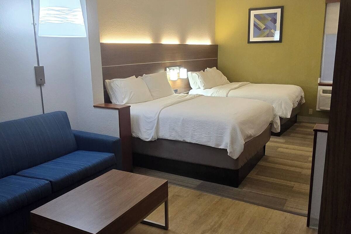Quarto de hotel com uma cama, um sofá, uma mesa de centro e uma luminária na parede.