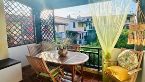 A small patio with a round wooden table and chairs, a potted plant, and a yellow cushion on a wooden chair.