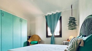 A bedroom with a bed, a wardrobe, a chair, a window with curtains, and a hanging light fixture.