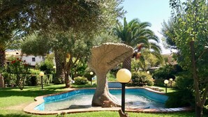 A garden with a swimming pool, surrounded by lush greenery and palm trees.