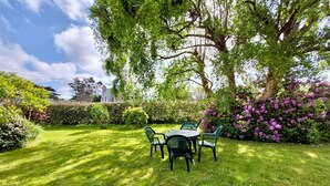 Un jardín bien cuidado con una mesa y sillas, rodeado de abundante follaje y arbustos florecientes.