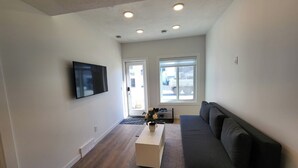 Ein modernes Wohnzimmer mit grauem Sofa, einem flachbildfernseher an der Wand und Holzboden.