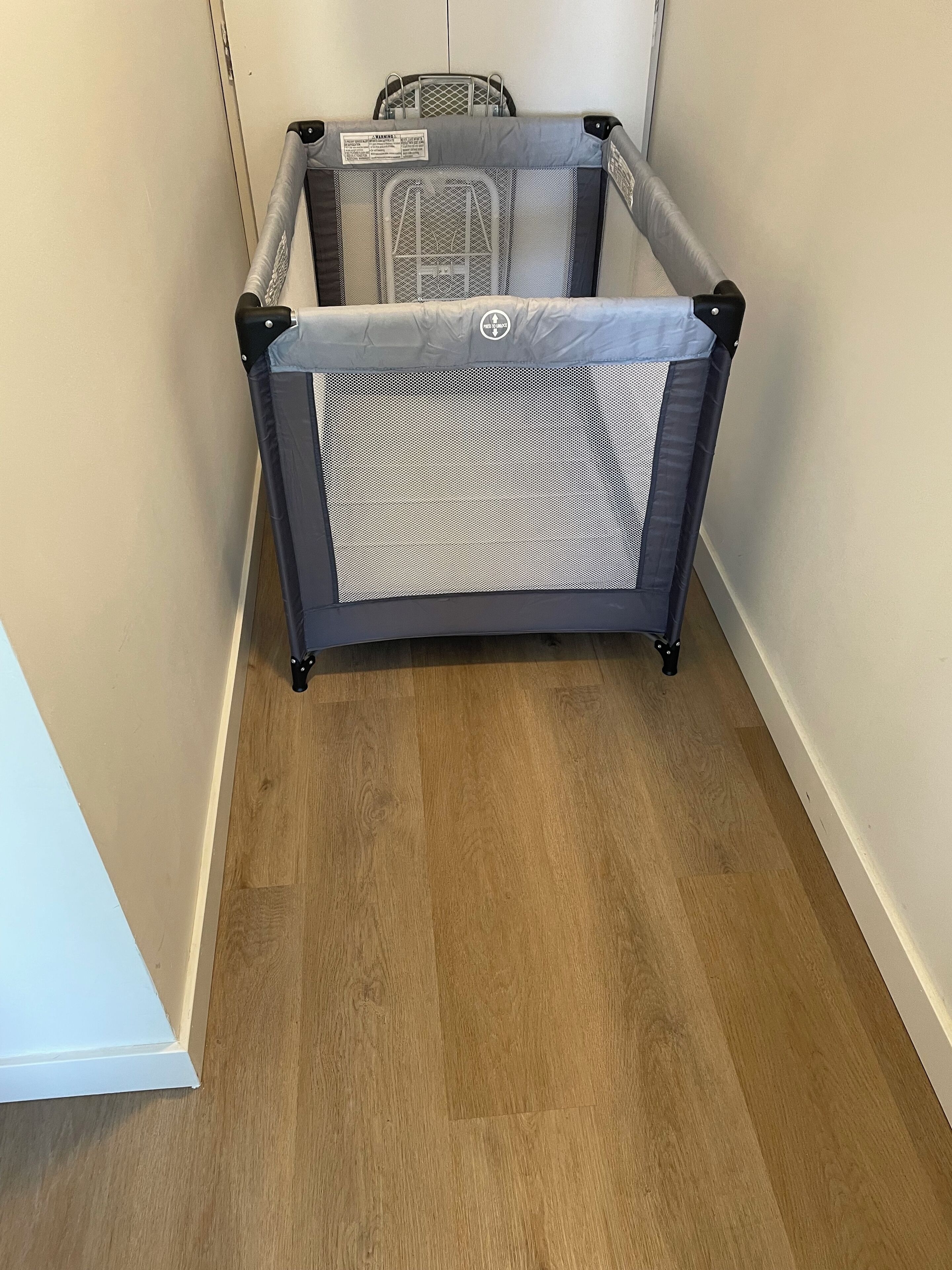 A room with a wooden floor, a grey playpen, and a white door.