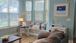 A living room with a television on a stand, a sofa, a small table, and a window seat with a lamp.