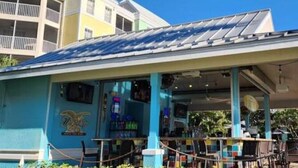 A building with a covered outdoor seating area, a blue exterior, and a palm tree in the background.