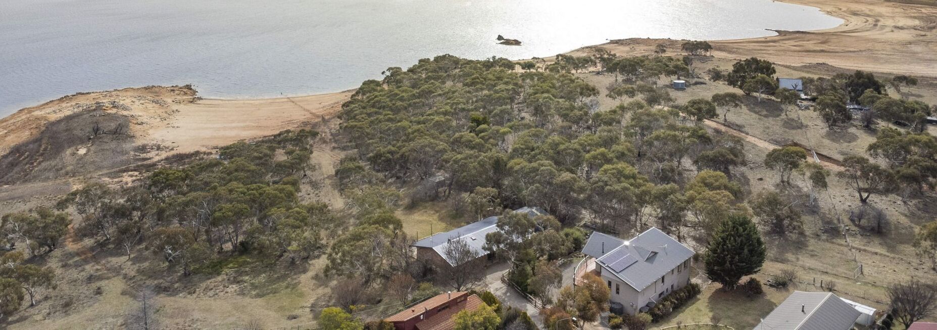 Vista aerea di una proprietà costiera con una casa circondata da fitta vegetazione e una spiaggia sabbiosa.