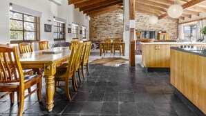 A spacious dining area with wooden tables and chairs, a stone floor, and a kitchen with wooden cabinets and a large island.