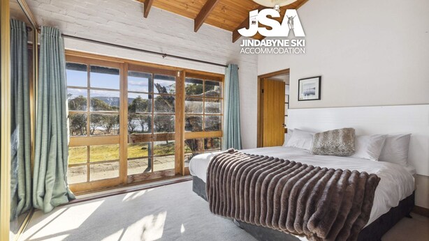 A bedroom with a large bed, a view through a sliding glass door, and a wooden ceiling.