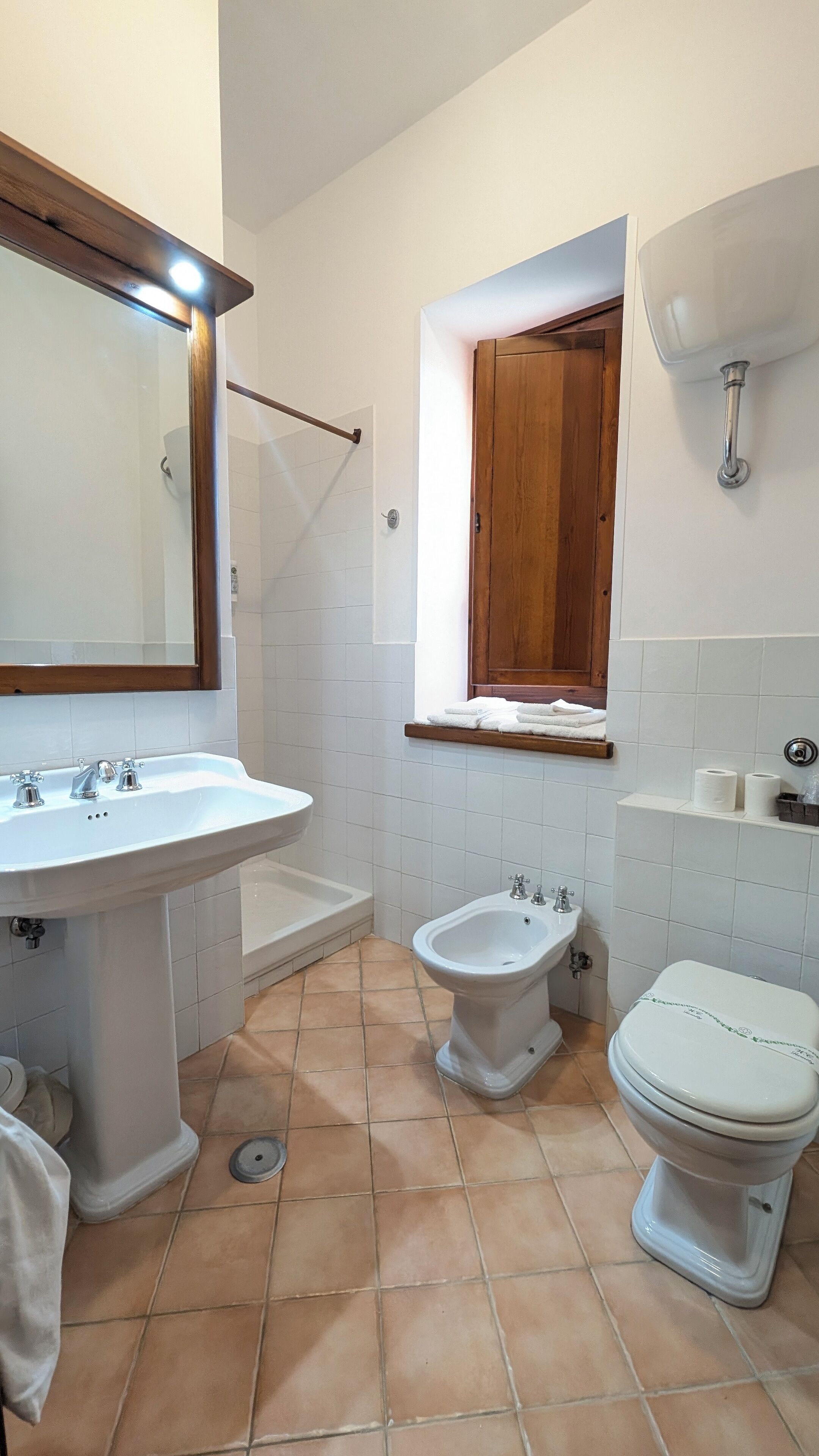 Un baño con lavamanos, bidé, inodoro y ventana con marco de madera.