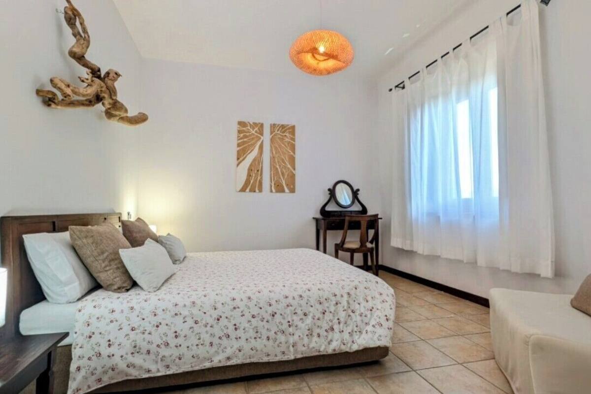 Un dormitorio con cama, mesita de noche, lámpara y una silla.