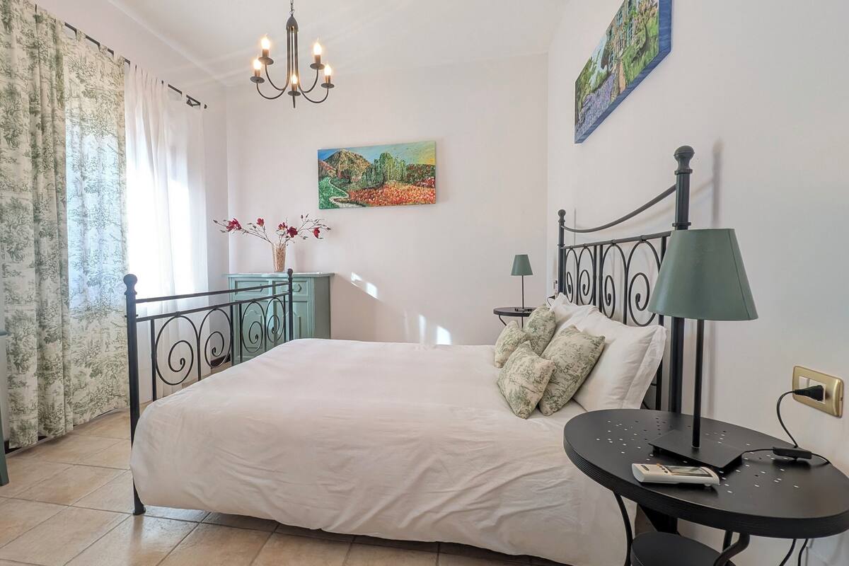 Un dormitorio con cama, escritorio, silla, candelabro y obras de arte en las paredes.
