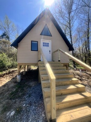 A wooden cabin with a triangular roof, a front door, and a set of wooden stairs leading up to the entrance.