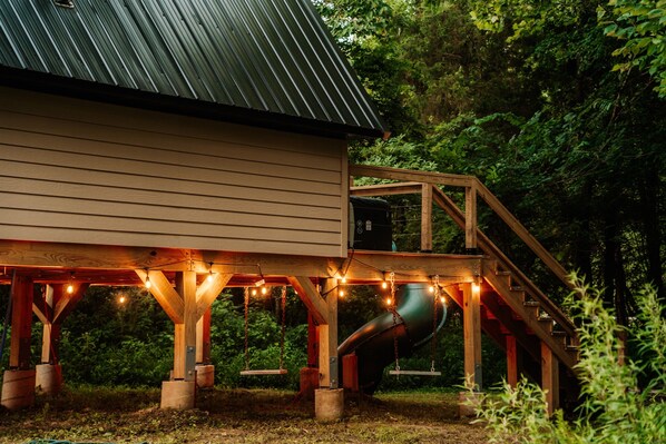 A wooden deck with a metal roof, a slide, and string lights.