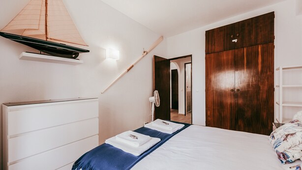 A bedroom with a bed, a wooden wardrobe, a white dresser, and a sailboat model on the wall. - Beach House By Gt House (Silves)