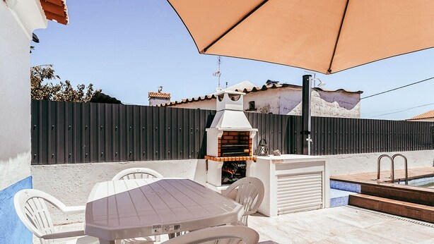 An outdoor patio with a table and chairs, a barbecue grill, and a swimming pool.