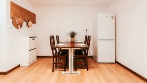 A dining area with a wooden table, four chairs, a small potted plant, and a white refrigerator.