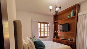 Un dormitorio con una cama, un televisor, un estante de madera y una ventana con cortinas.