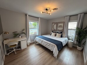 Quarto com cama, escrivaninha, cadeira e plantas em vasos.