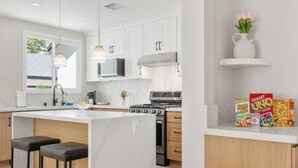A modern kitchen with white cabinets, a central island with stools, a stove, and a microwave. - Elegant Oasis | Heated Pool & Spa | 5mi to Beach (Long Beach)