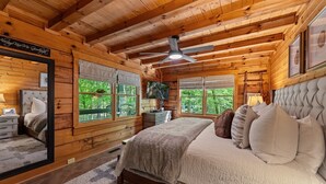 A wooden cabin bedroom with a bed, a nightstand, a dresser, a ceiling fan, and large windows. - *Riverhouse on the Cartecay*WaterFront~Tube~Family (Ellijay)
