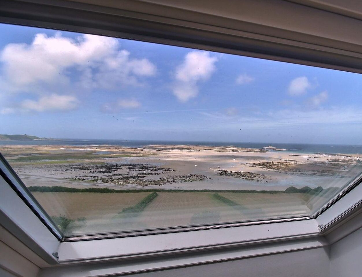 A view from a window overlooking a coastal landscape with sandy areas and vegetation.
