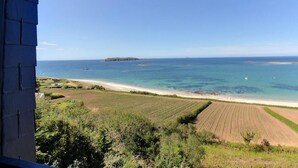 Vista costera con playa, tierras de cultivo y una isla distante.
