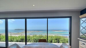 Una habitación con ventanas de gran altura que ofrecen vistas al mar y una isla distante.