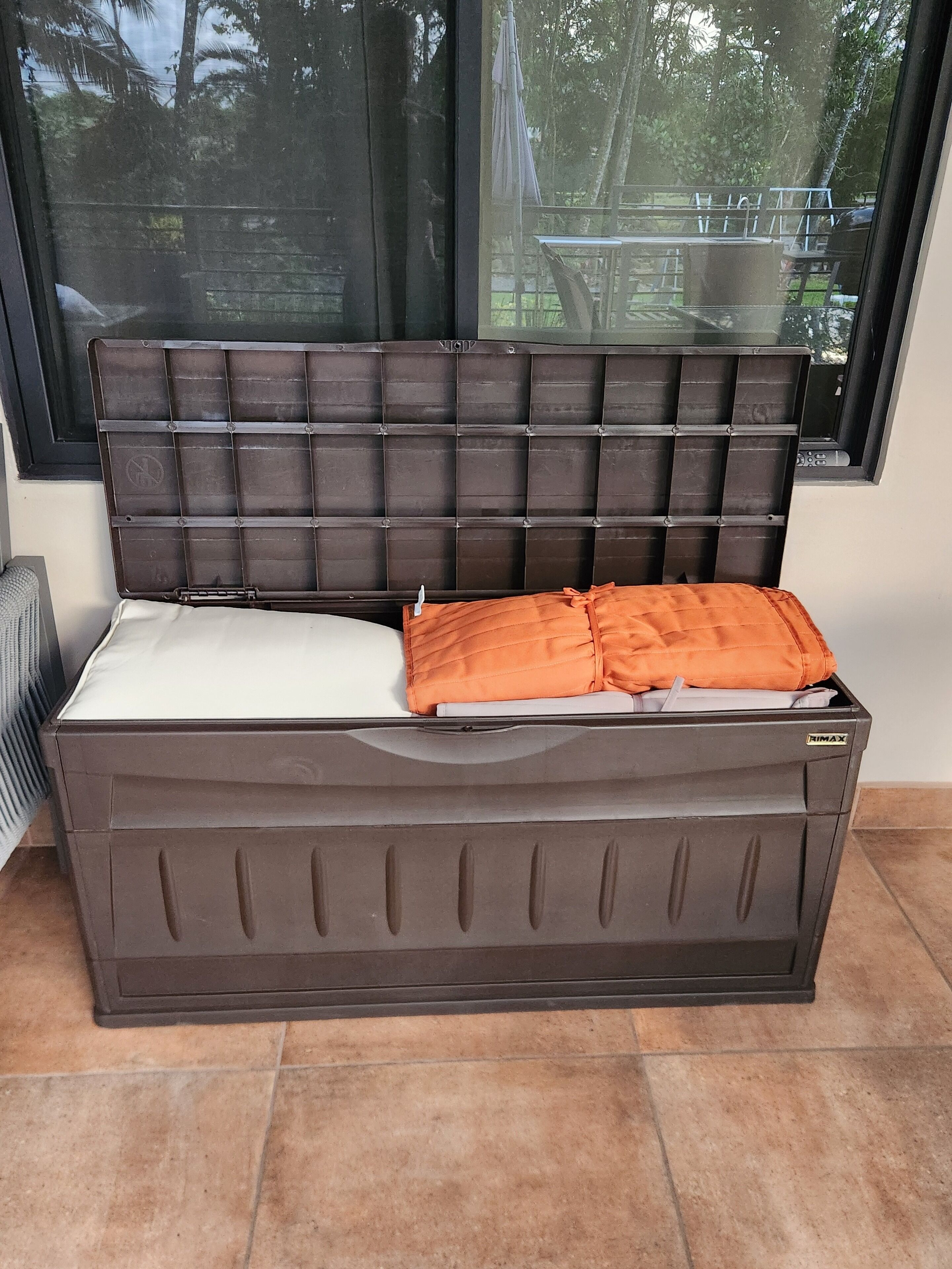 Un canapé marron doté d’un repose-tête rembourré et d’un coussin blanc, placé dans une pièce avec une fenêtre donnant sur des arbres.