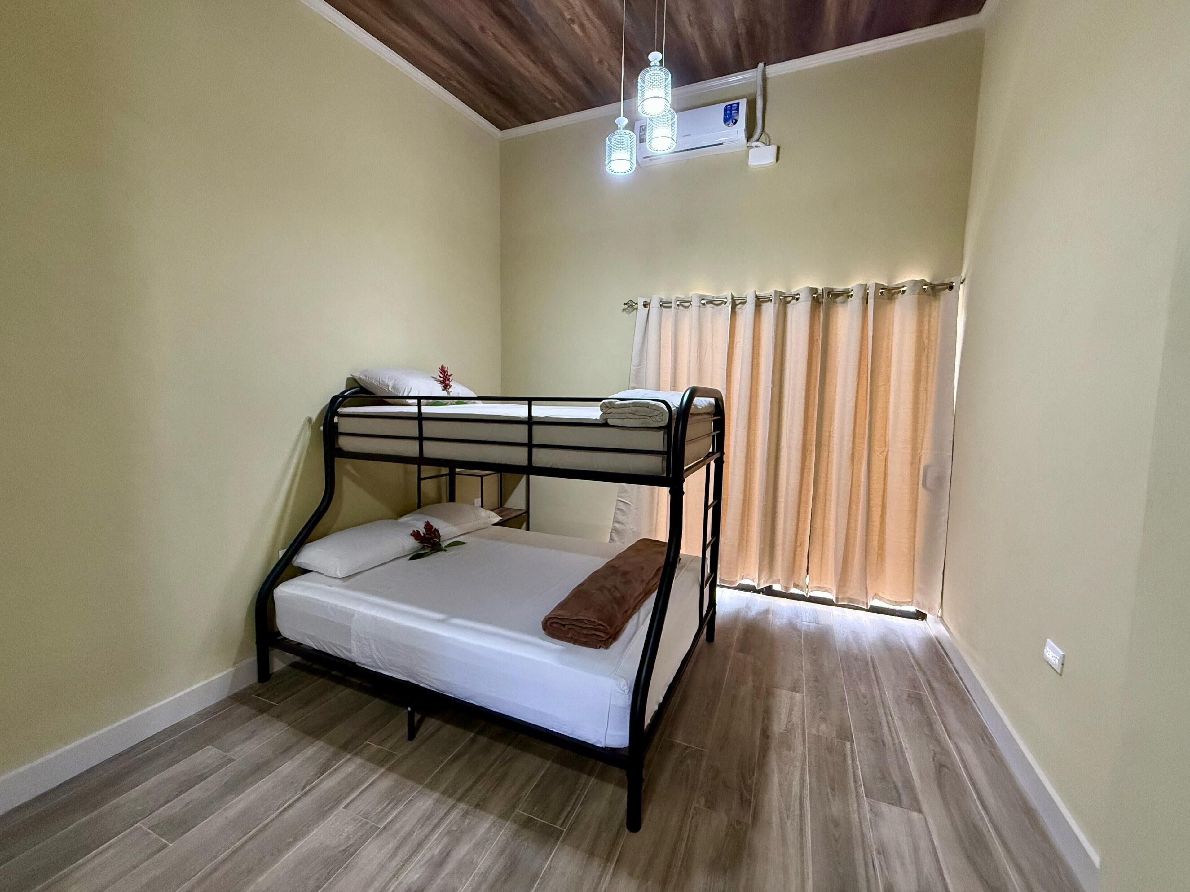Habitación con literas, techo de madera, aire acondicionado y ventana con cortinas.