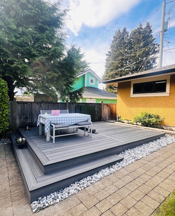 Une terrasse en bois avec un banc et une table, entourée d’une clôture en bois et avec une maison en arrière-plan.