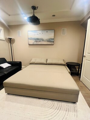 Een slaapkamer met een groot bed, een zwarte bank, een kleine tafel en een schilderij aan de muur.