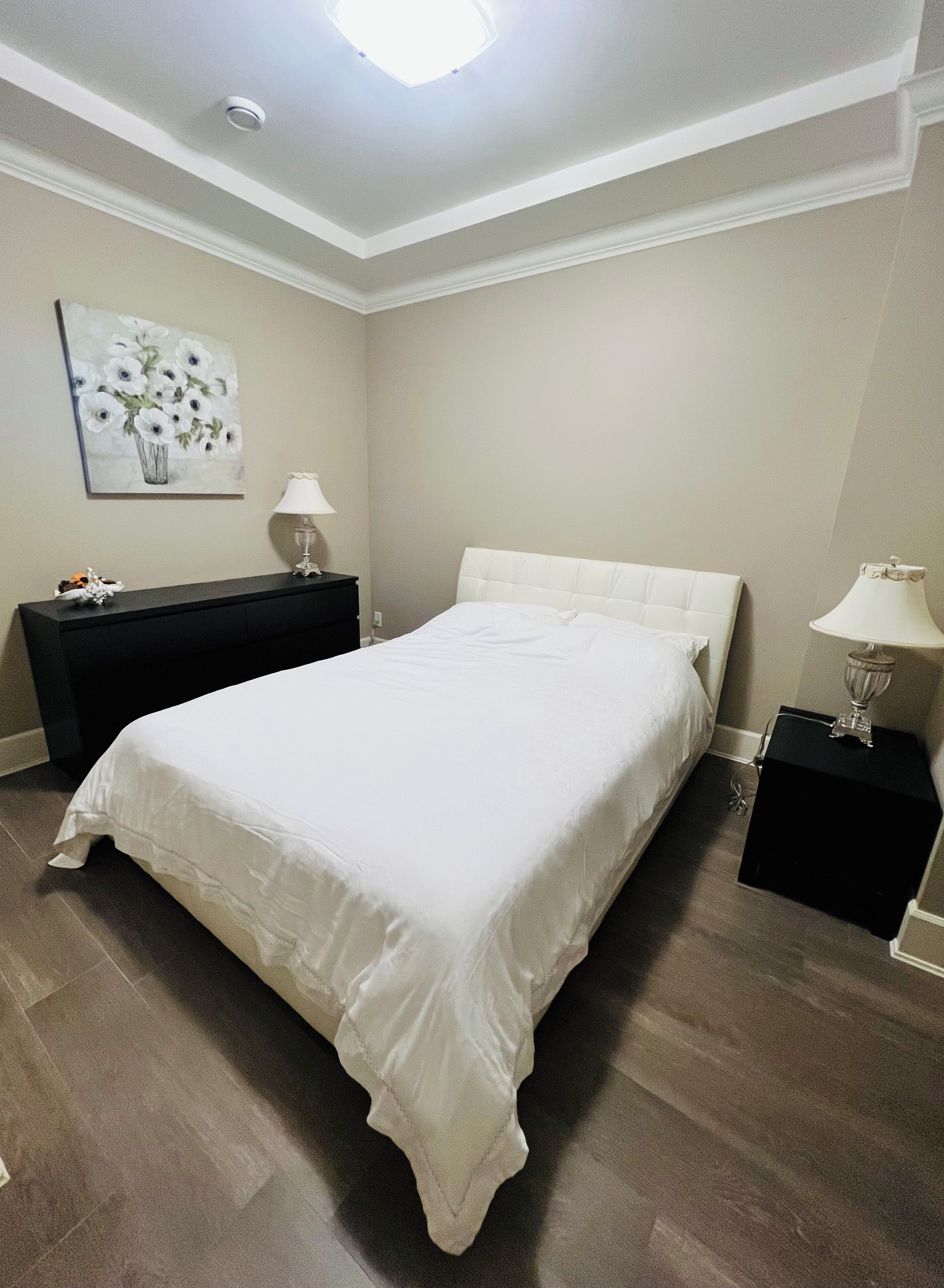 A bedroom with a large bed, a dresser, a nightstand, a lamp, and a painting on the wall.