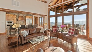 A spacious living room with a large window offering a mountain view, a stone fireplace, and a kitchen area with modern appliances.