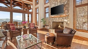 A spacious living room with a stone fireplace, leather furniture, and large windows offering a mountain view.