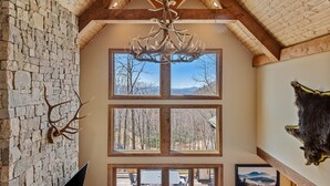 A spacious interior with a stone wall, a chandelier, and multiple windows offering views of the outdoors. - Rock Haven at Eagles Nest - pets, views, four king beds, hot tub (Banner Elk)
