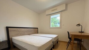A bedroom with two single beds, a desk with a chair, a window, and a ceiling fan.