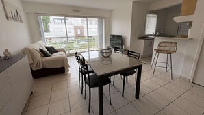 A modern living room with a sofa, a dining table, and chairs. There is a large window providing a view of the outside.