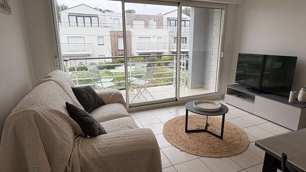 A modern living room with a sofa, a TV, and a view of a residential area through large sliding glass doors.