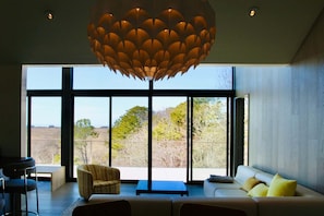 Un salon moderne doté d’une grande fenêtre, d’un canapé, d’un fauteuil et d’un luminaire au plafond au design original.