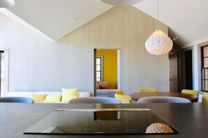 Ein modernes Interieur mit Essbereich, einer Couch mit Kissen, einem Tisch und einer Pendelleuchte.