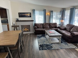 Una sala moderna con chimenea, sofá de cuero, mesa de comedor y un gran ventanal con cortinas.
