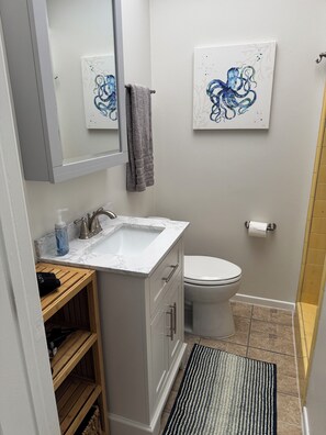 Features a sleek sink, toilet, and large mirror, with a wooden shelf and abstract artwork.