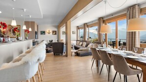 Amplia sala de estar con mesa de comedor preparada para seis personas, un sofá y un gran ventanal con vistas a la montaña.