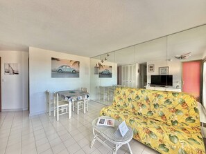 Una sala de estar con sofá, una mesa de comedor con sillas, televisor y obras de arte en las paredes.