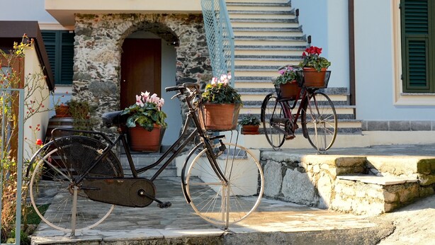 A bicycle with baskets, a stone archway, and a staircase leading to a balcony.