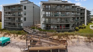 Ein mehrstöckiges Wohngebäude mit Balkonen, einer Holzterrasse und einer Sandstrandfläche.