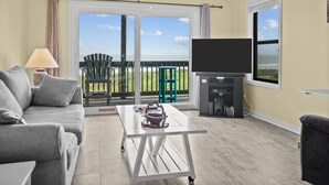 Ein Wohnzimmer mit Sofa, Couchtisch, Fernseher und einem Balkon mit Blick.
