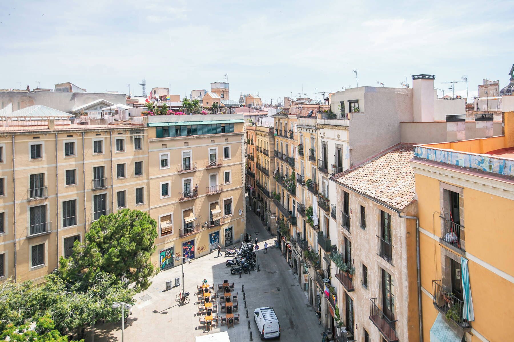 A narrow street with buildings on both sides, featuring balconies and a row of outdoor seating.