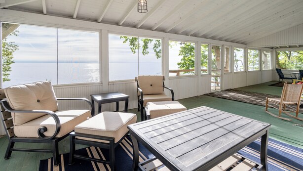 A covered outdoor seating area with a view of the water, furnished with chairs and tables.
